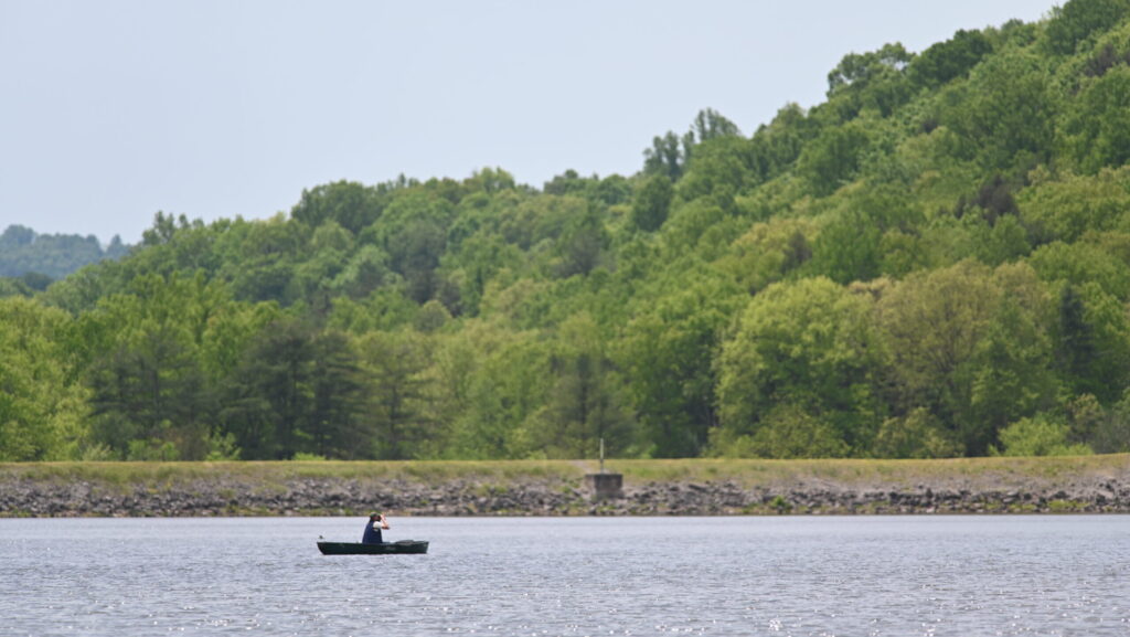 A person in a small boat floats near the damn in Lake Perez