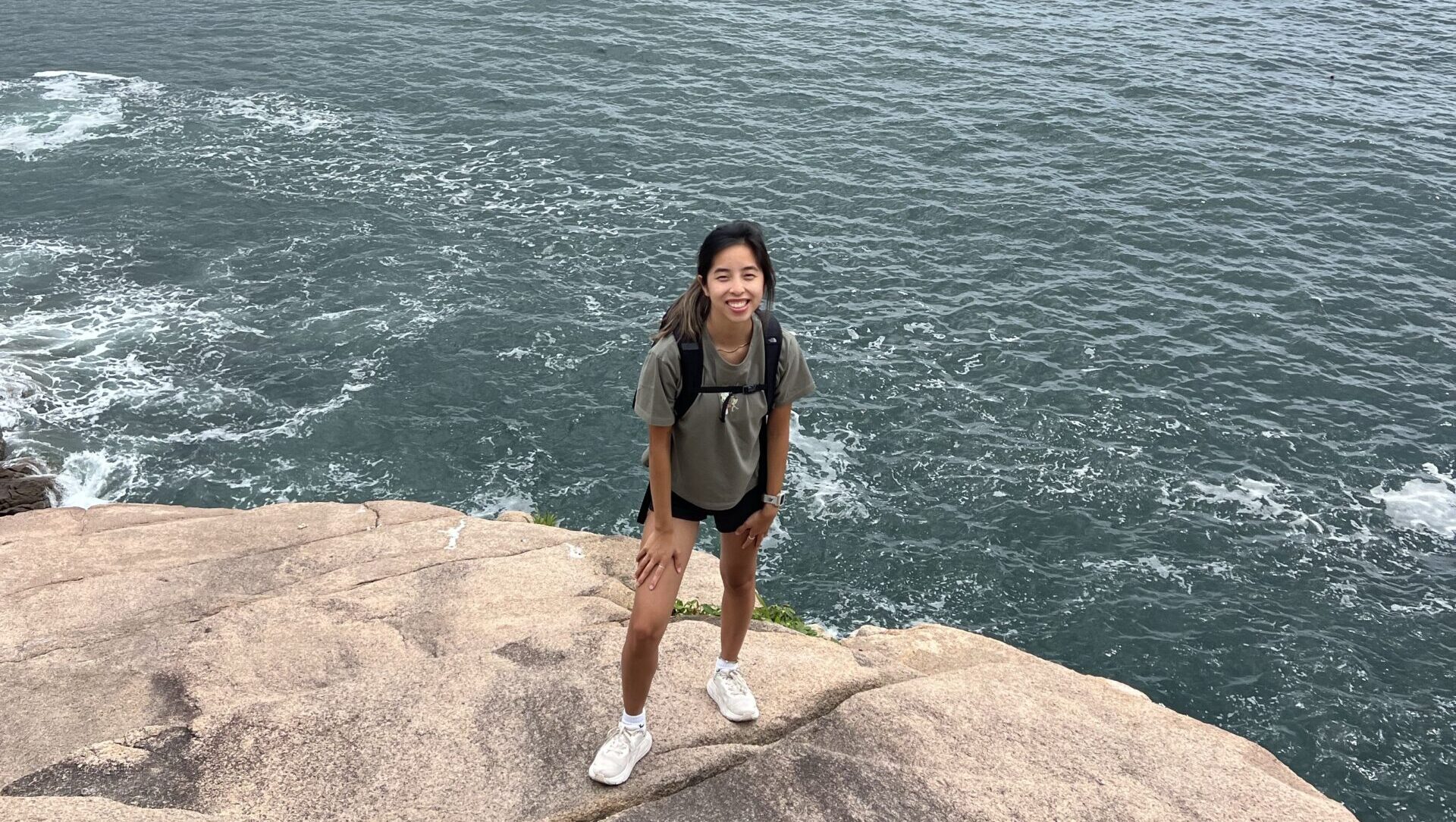 Lydia standing on a rock at the edge of a large body of water.