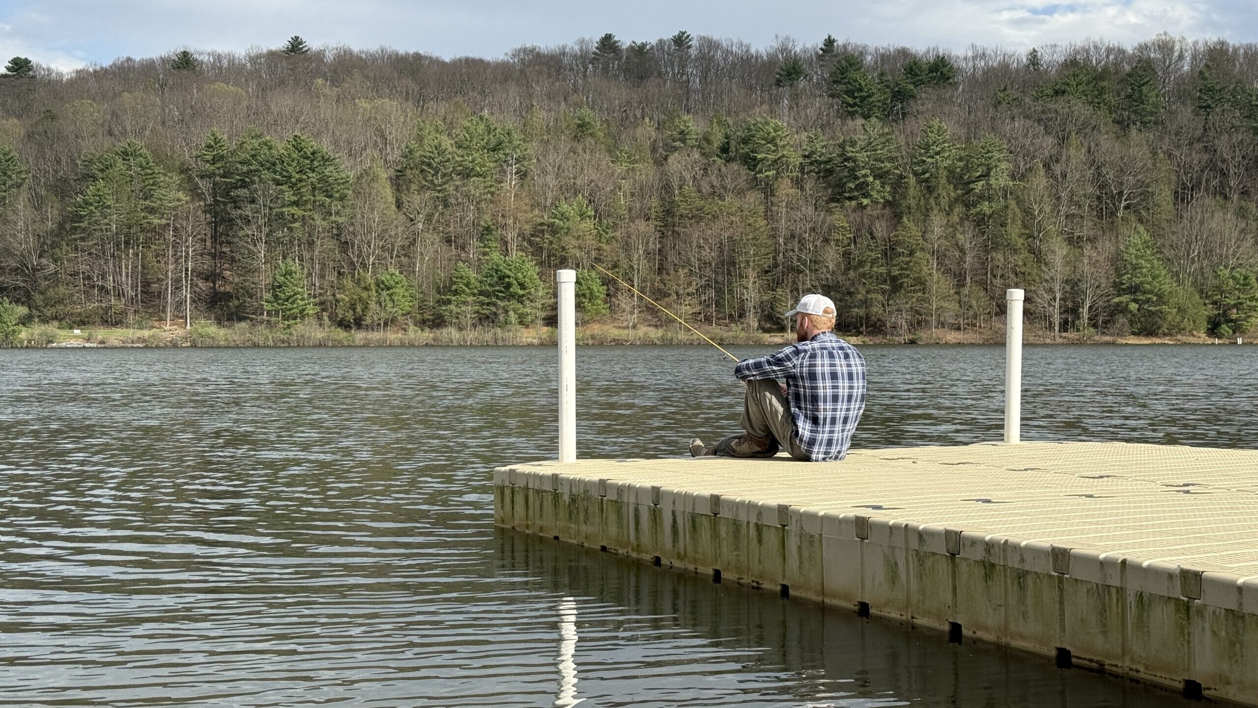 Someone sits at the end of a dock overlooking a lake.