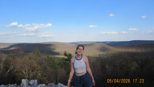 Yael posing at a rocky outcropping on a ridge in central Pennsylvania. The valley below shows forest and fields.