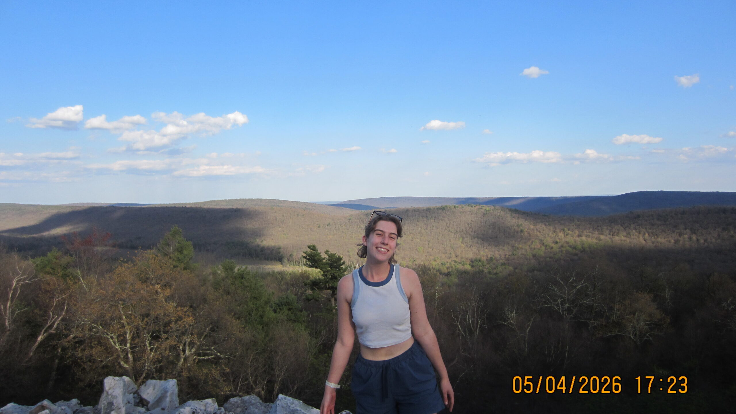 Yael posing at a rocky outcropping on a ridge in central Pennsylvania. The valley below shows forest and fields.