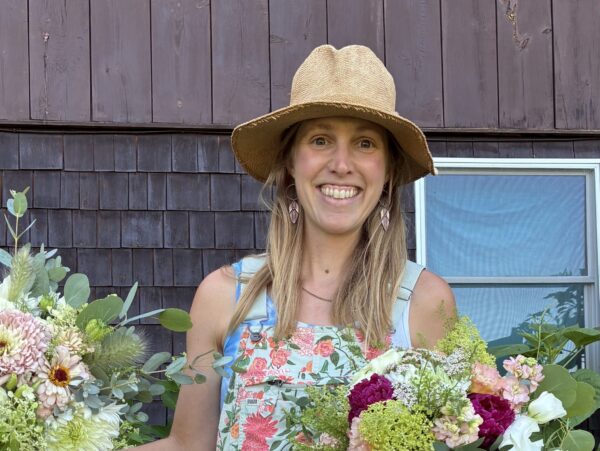 Dana wearing floral overalls and holding large bouquets of flowers.