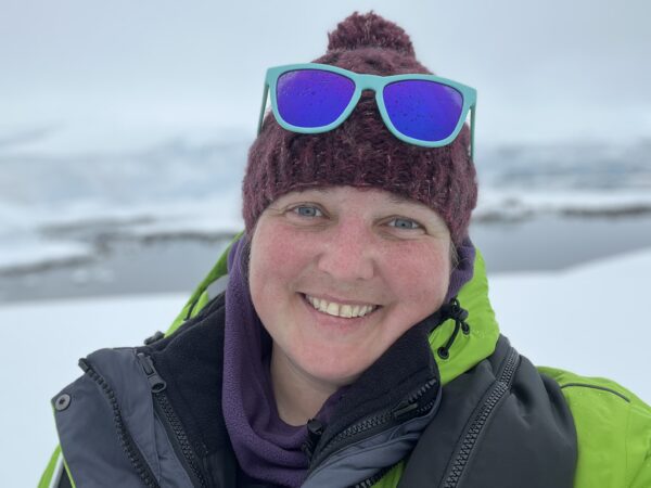 Allison wearing a beanie and a winter coat and standing in front of a frozen creek.