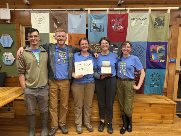 Five birders stand in front of quilted wall hanging holding a bird watching award