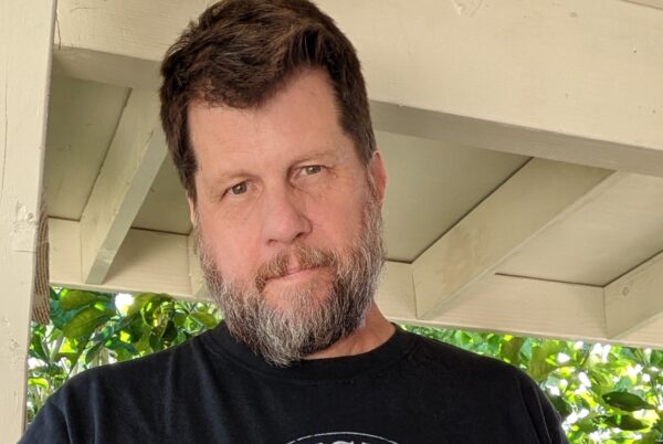 Buck standing under the overhang of a porch, wearing a black t-shirt.