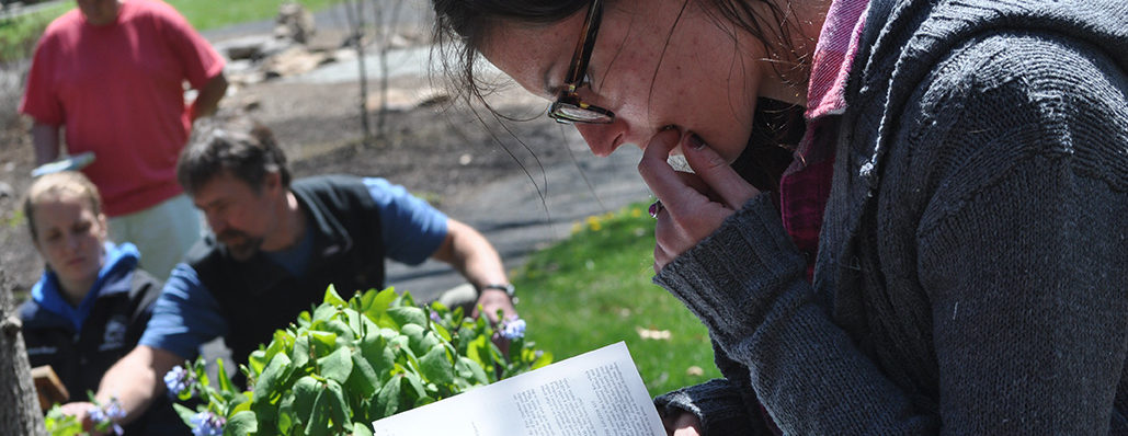 A graduate student references a book as fellow students work in a garden in the background