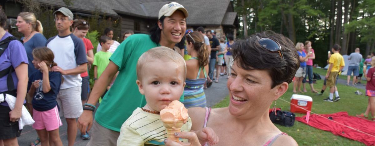 A toddler's mom helps him eat an ice cream cone during a Shaver's Creek event