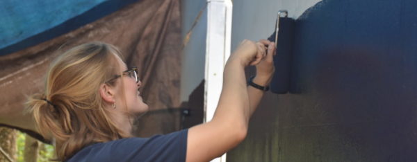 A volunteer applying a fresh coat of black paint to a wall