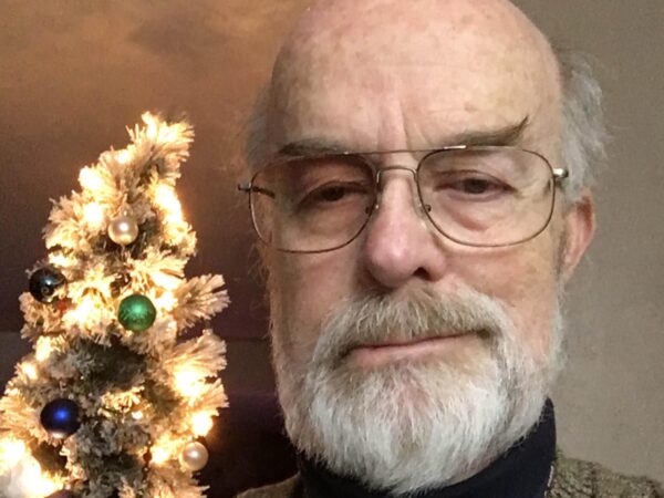 Closeup of Mark W. McBride in front of a white tree decorated with colorful round ornaments