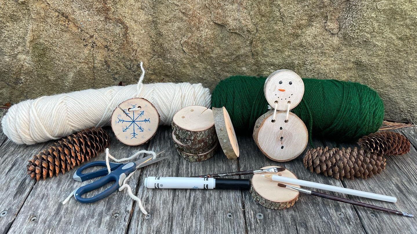 Supplies for making a wood cookie, including yarn, small circles of wood, markers, and scissors.