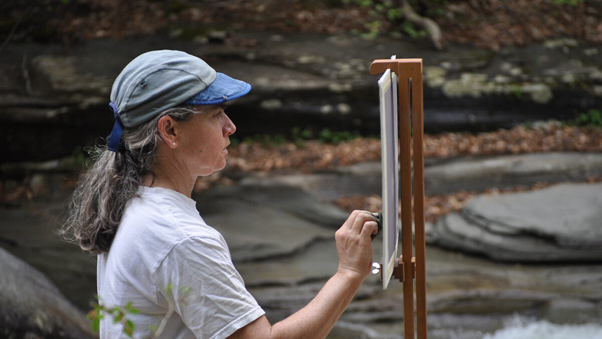 Alice Kelsey painting a canvas beside a stream