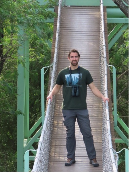 Andrew Bechdel standing on a suspension bridge in a forest