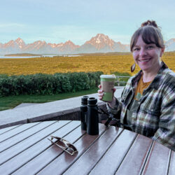 Lisa Hayes enjoying a hot beverage at a table with a view of mountains in the distance.
