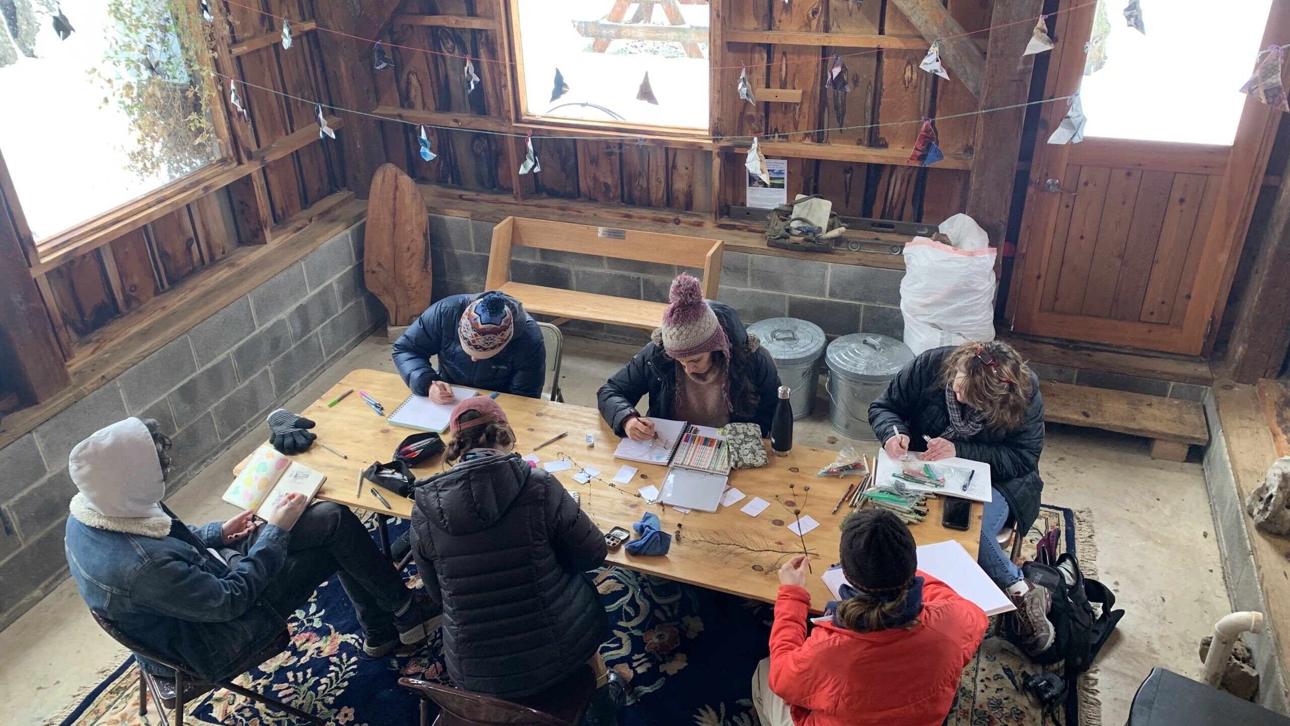A group of people sit around a wooden table and work on nature journals