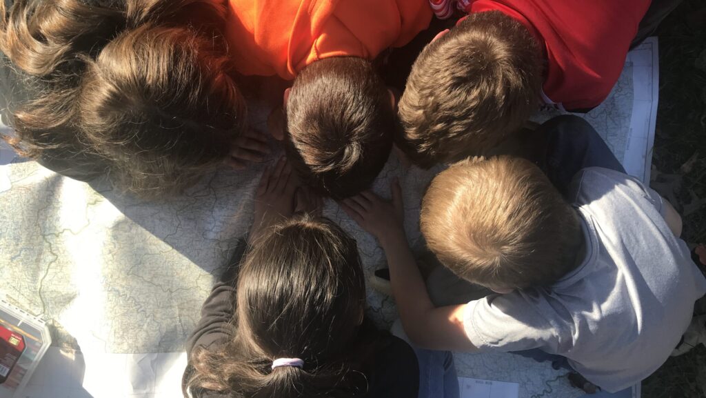 Young children put their heads together to study a map closely