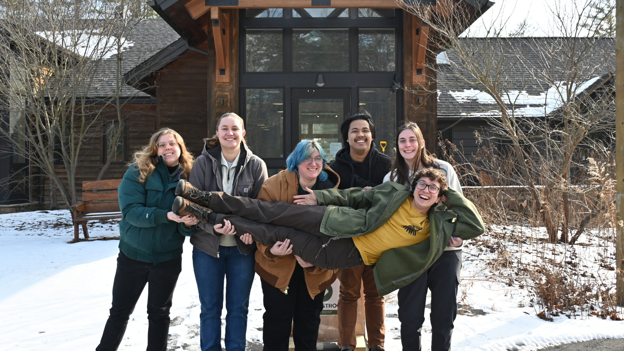 A group of interns hold the author up outside the entrance of the Shaver's Creek visitor center