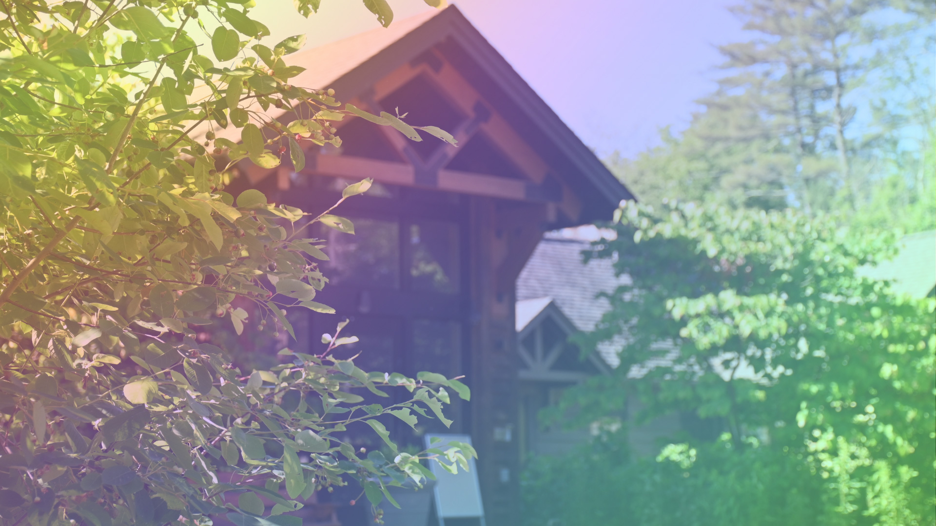 A wooden building surrounded by trees and bushes; a rainbow is overlayed.