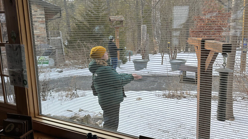Two people stand still in the cold near bird feeders, trying to get birds to come near