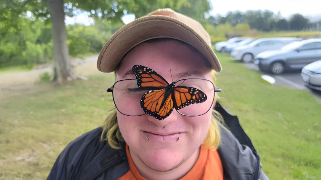 A person with a monarch butterfly perched on their glasses