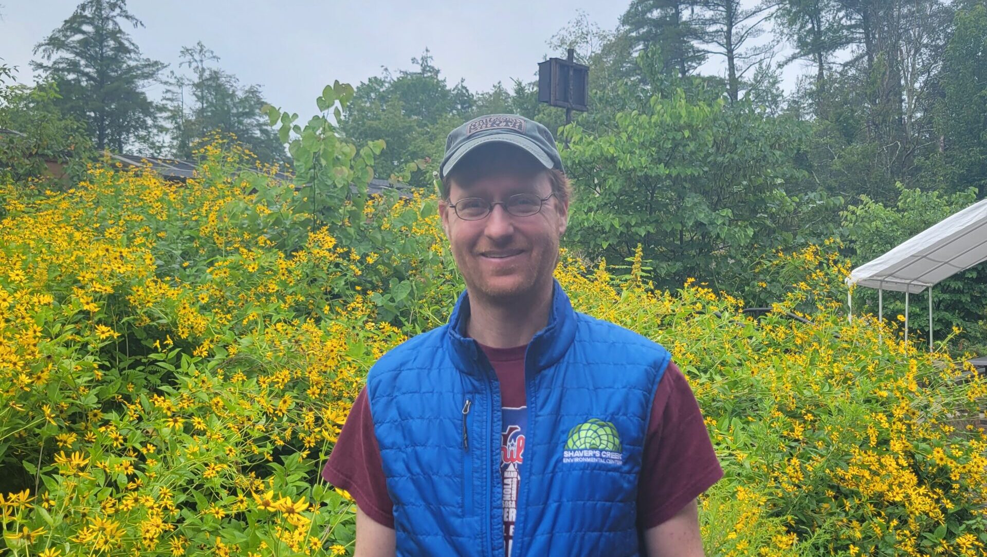 Matt standing in front of yellow flowers and wearing a blue Shaver's Creek vest.