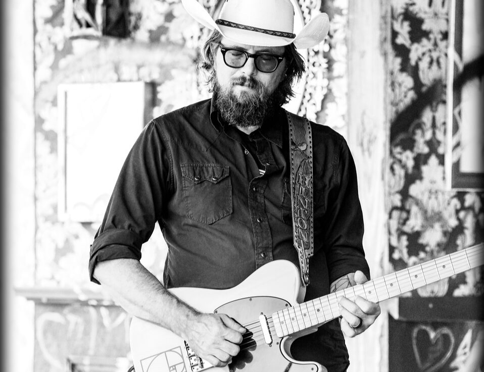 Brad wearing a cowboy hat and glasses and playing a guitar.