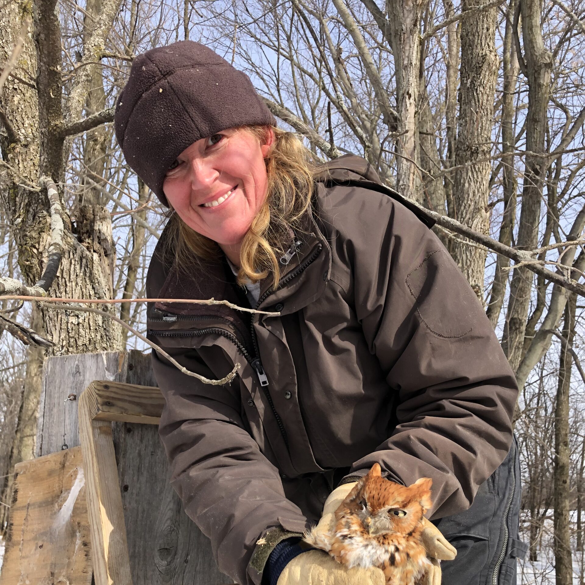 Toni wearing a winter hat and leather gloves and holding a small owl.
