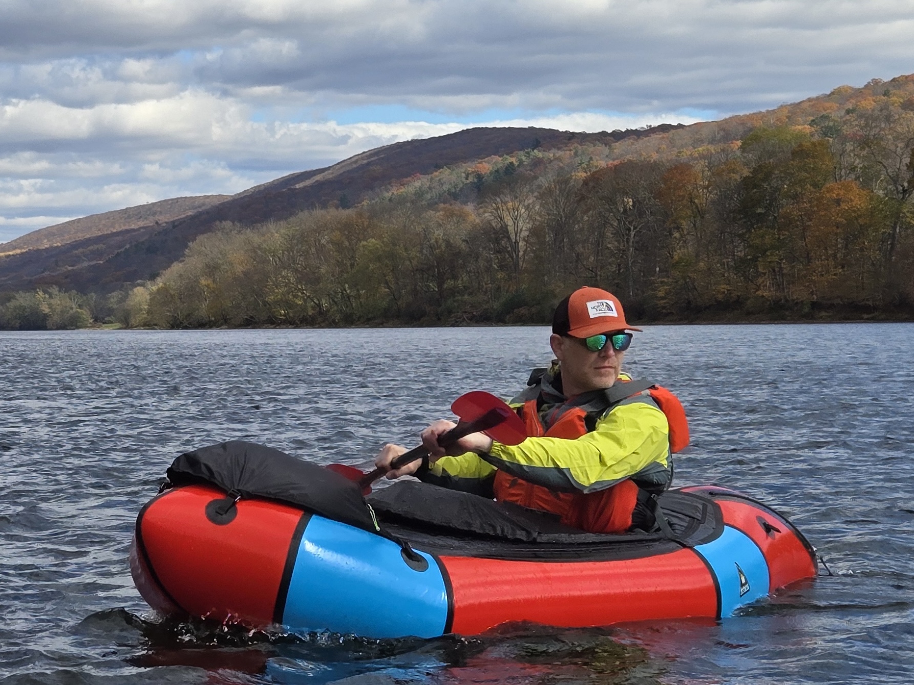 Jason paddles an inflatable raft across a lake with mountains in the background.