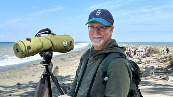 A man wearing a baseball cap smiles at the camera at the beach