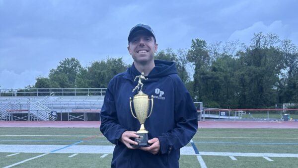 Joseph standing on a sports field and holding a trophy.