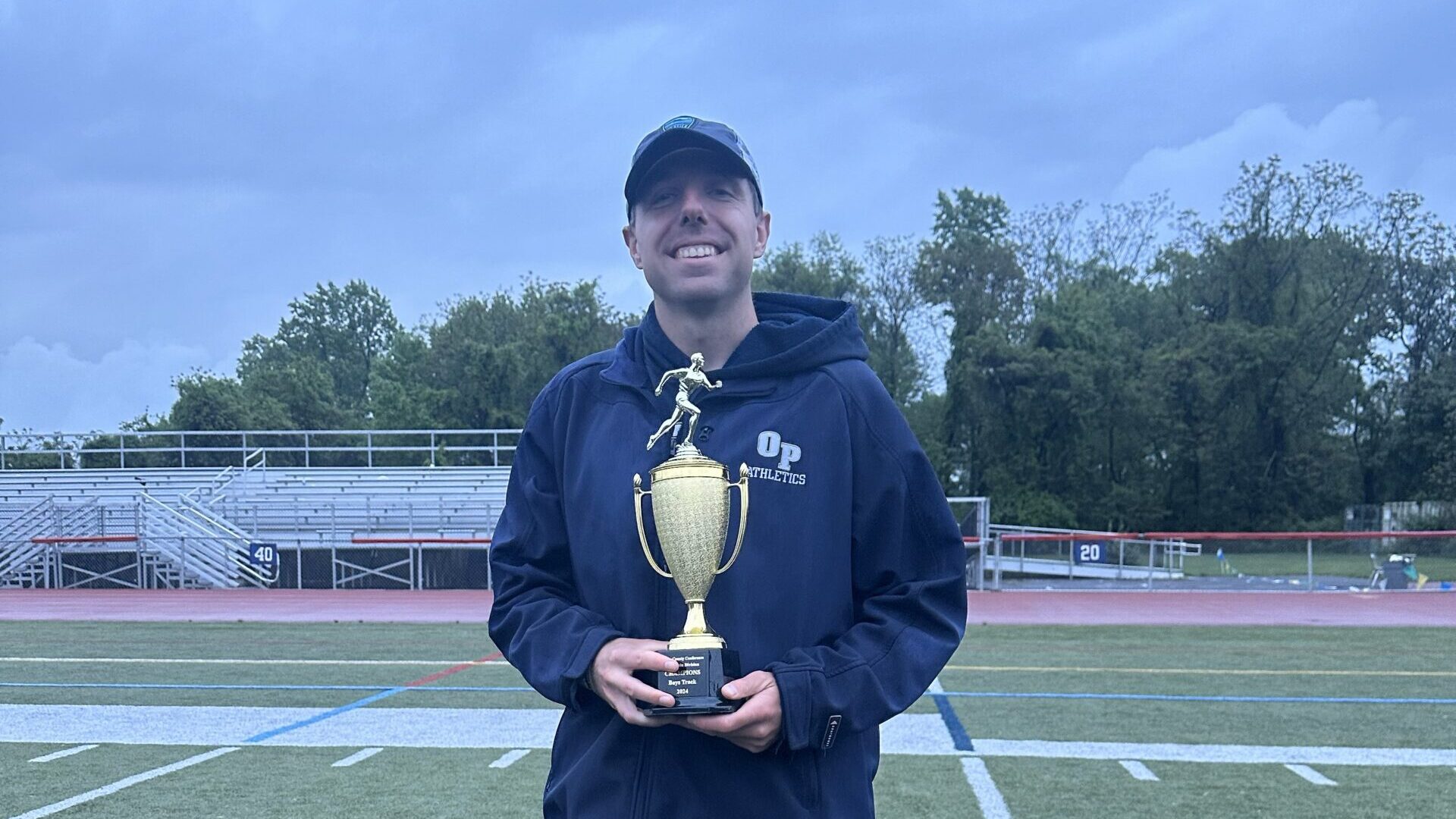 Joseph standing on a sports field and holding a trophy.