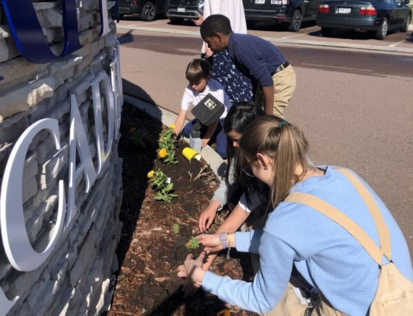 Sierra planting marigolds in front of a sign.