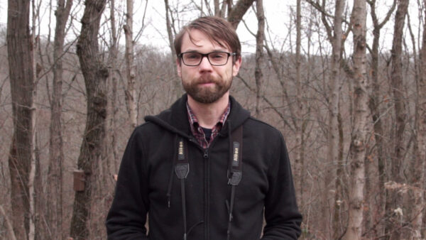 Matthew Shumar stands in the winter woods wearing binoculars around his neck.