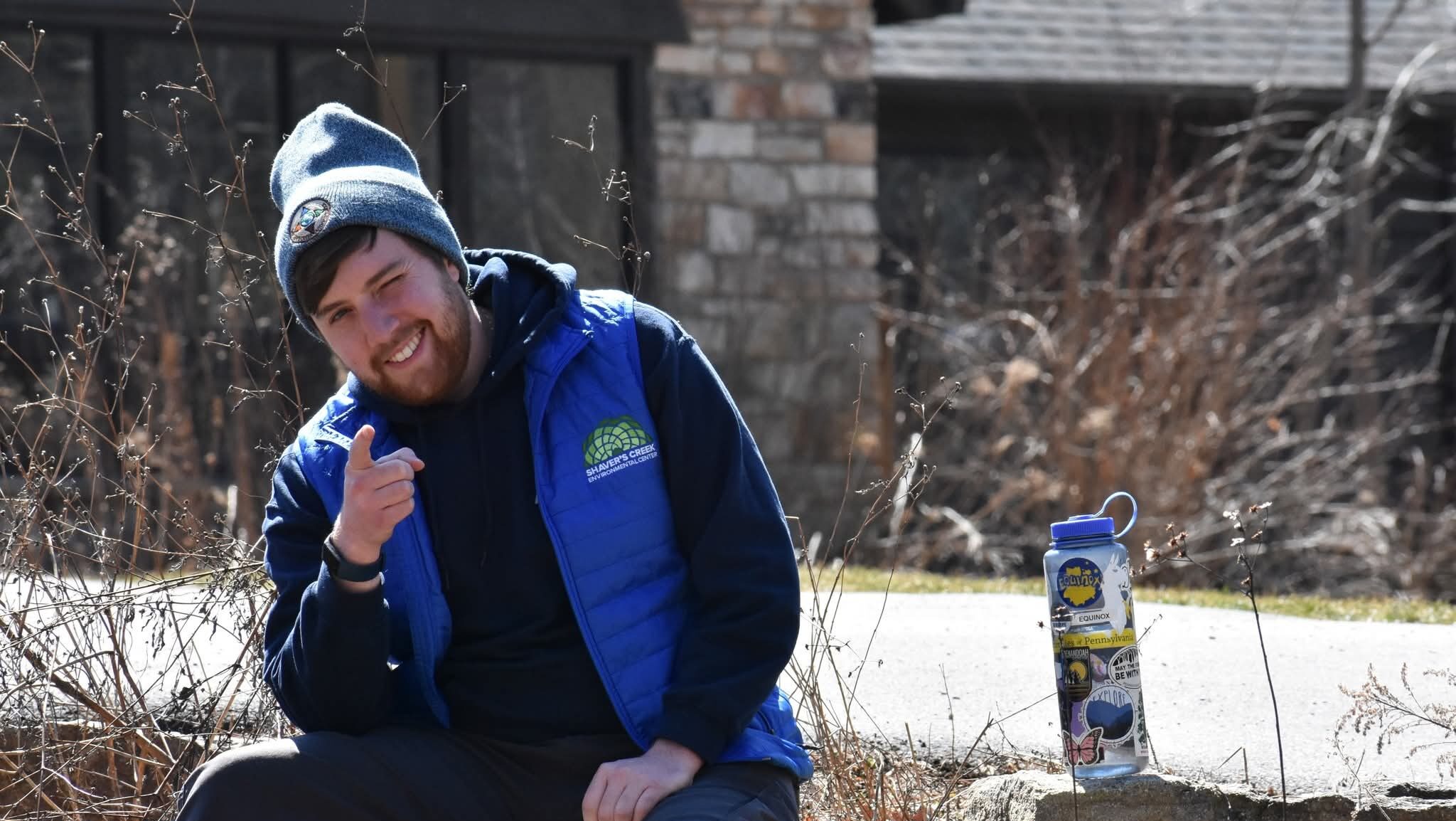 Tommy wearing a blue Shaver's Creek vest and sitting on a rock wall outside the visitor center.