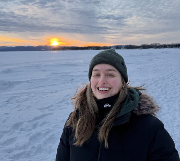 Lexi standing in a snowy field as the sun sets behind her