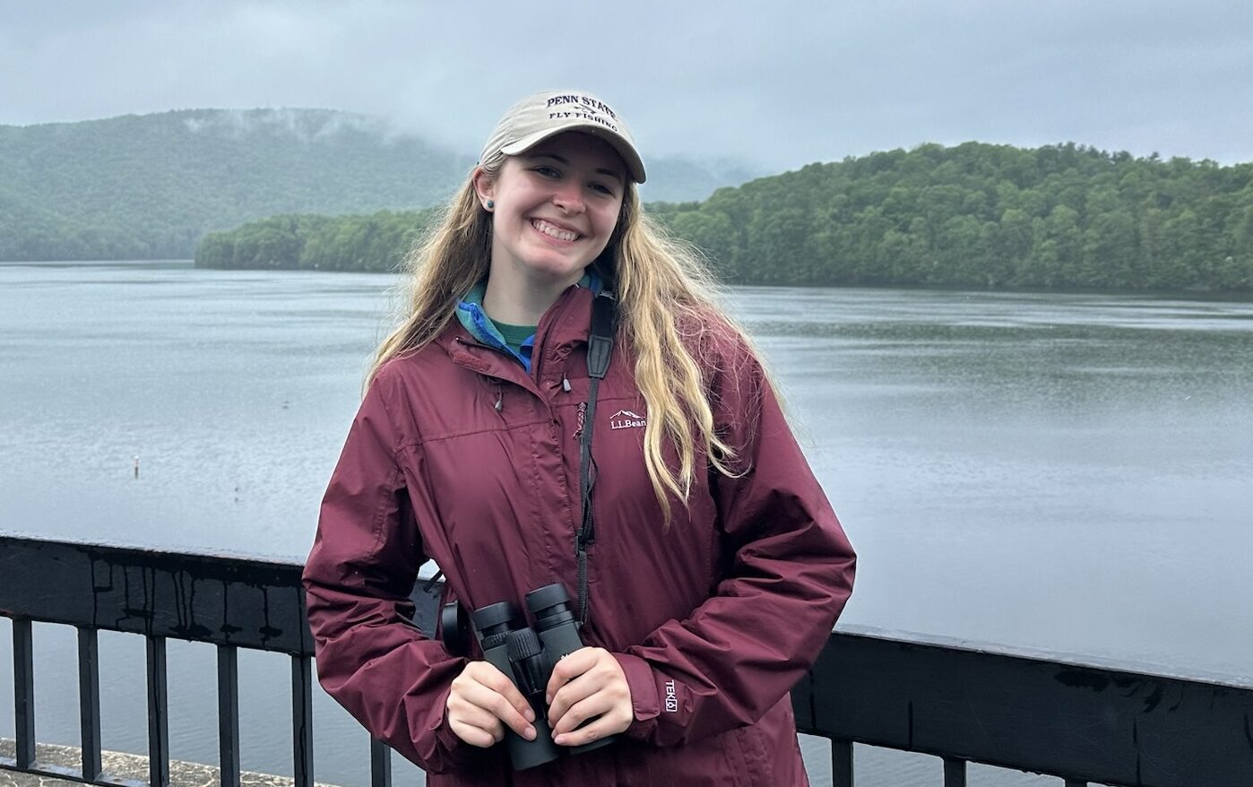 Samantha standing on a wooden deck overlooking a foggy lake, holding binoculars.