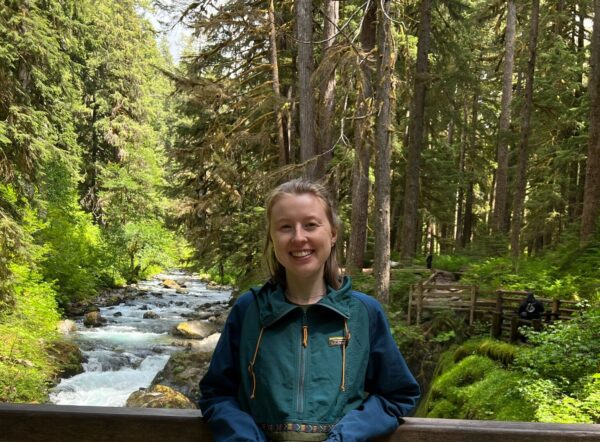 Katie standing on a wooden bridge with trees and a creek in the background.