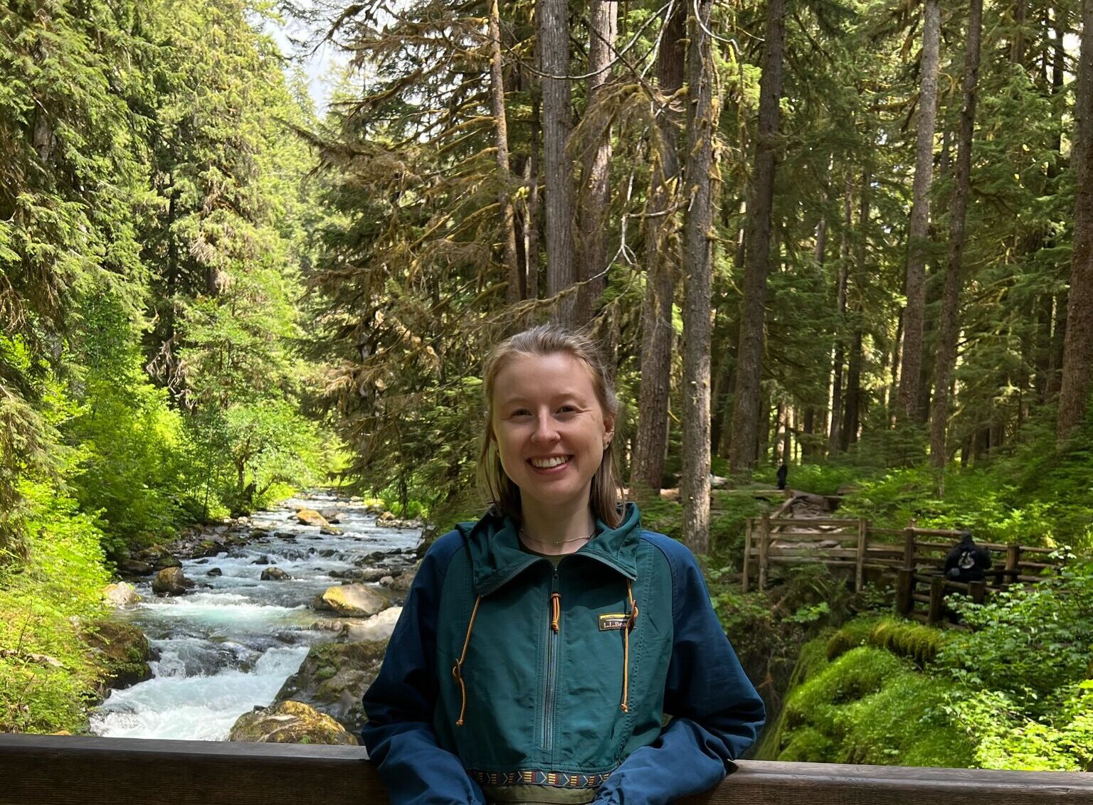 Katie standing on a wooden bridge with trees and a creek in the background.