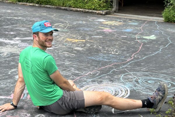 Isaac sitting on pavement surrounded by colorful chalk drawings.