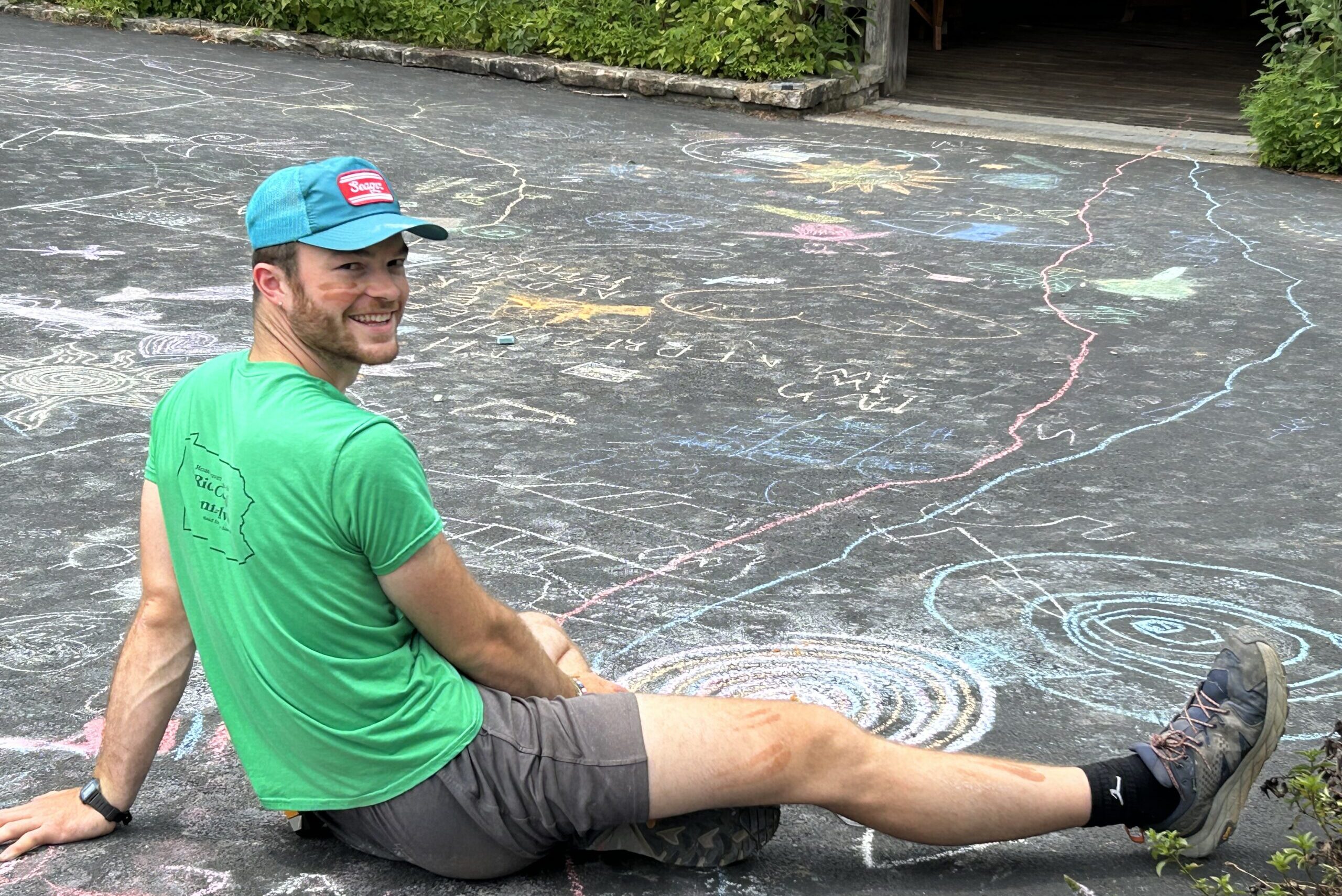 Isaac sitting on pavement surrounded by colorful chalk drawings.