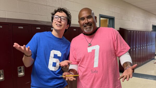 Andy, wearing a shirt with a 6 on it, stands beside a friend who is wearing a shirt with a 7. The two are holding their hands up, in reference to the popular 6-7 meme.