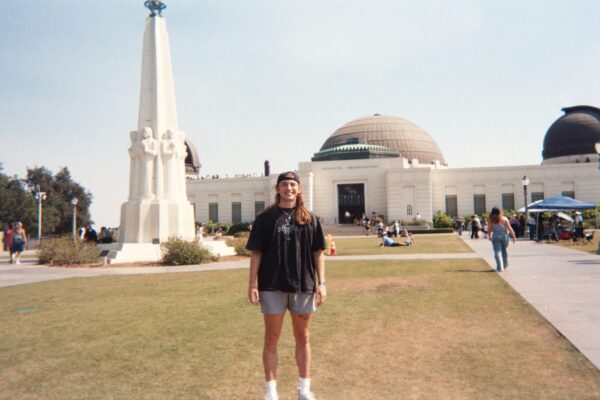 Joelian standing in front of a domed white building with a white monument in front.