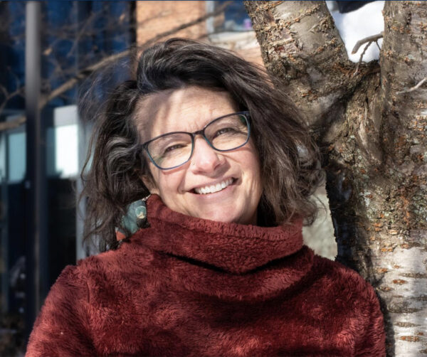 Jen wearing a turtleneck sweater and smiling under a tree.