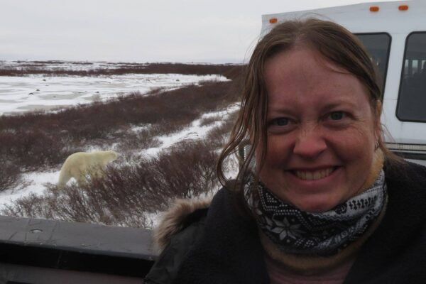 Janet standing in a field with snow and a polar bear in the background.