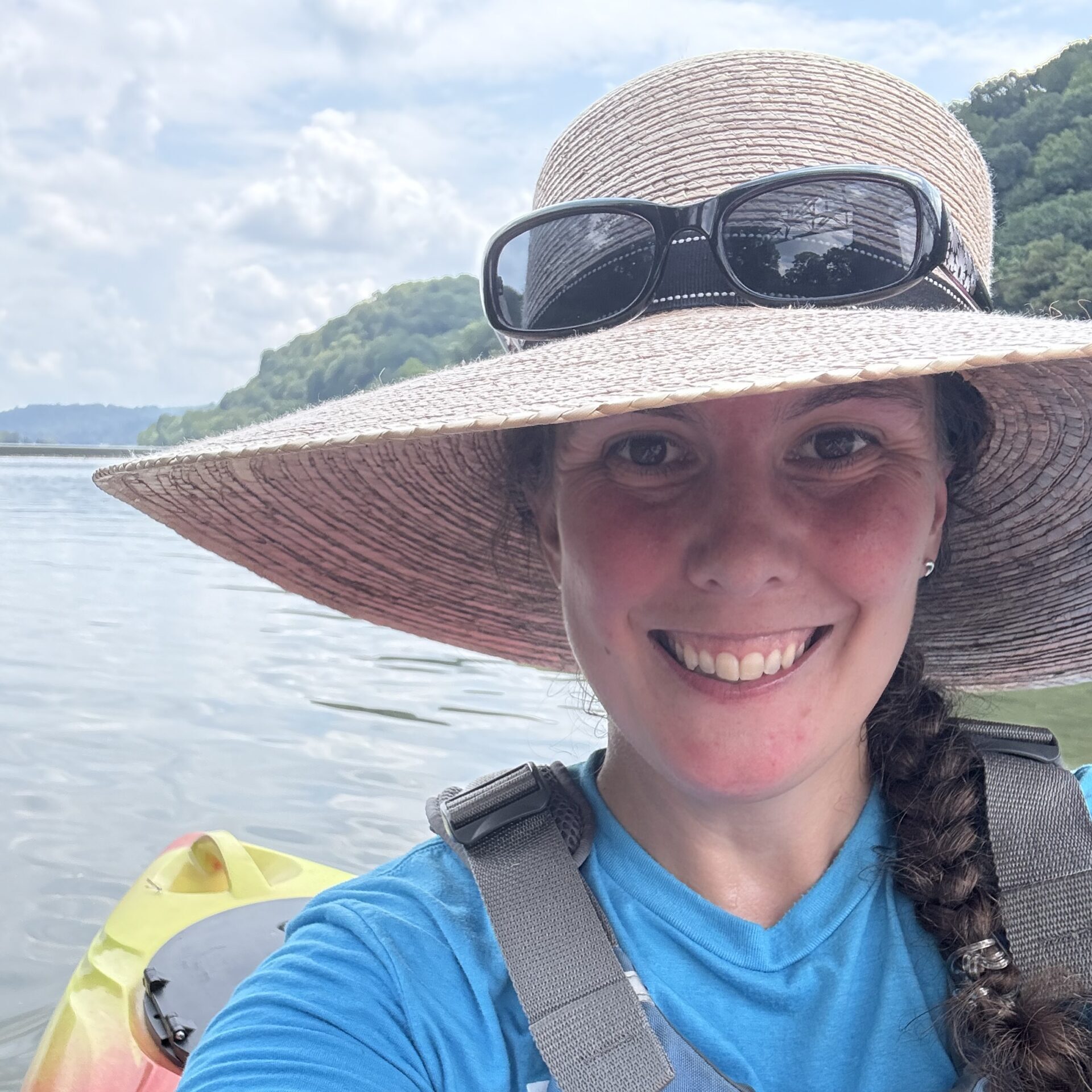 Sara in a kayak wearing a wide-brimmed sun hat and a personal flotation device.
