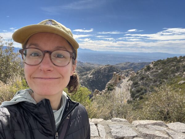 Alexa standing at an overlook with blue sky and low mountains in the background.