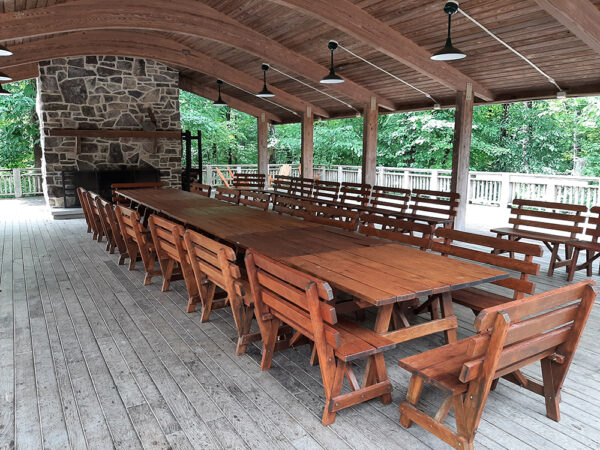 The Outdoor Classroom set up with square tables pushed together to make one long conference table with wooden benches on all sides.