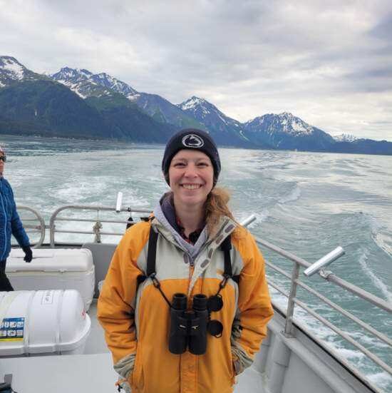 Allison standing on a boat in open water with snow-capped mountains in the distance.