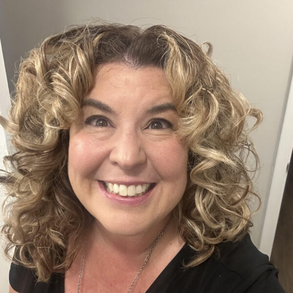 Jamie with curly hair and a black v-neck shirt, smiling.