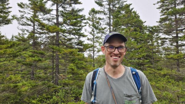 Mike stands in a forest with a backpack on his back.