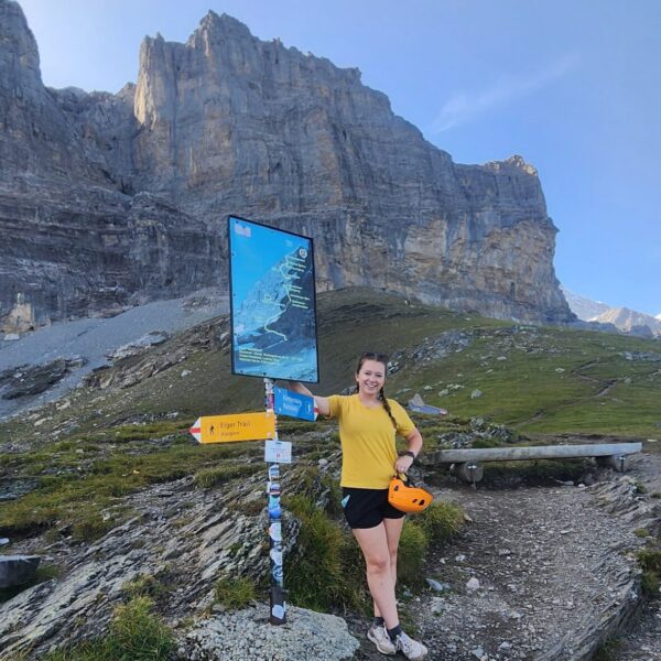 Kelly standing by a sign-post that marks a trail through rocky outcroppings.
